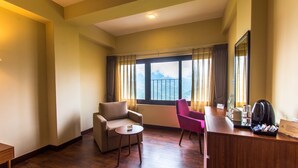 A hotel room with a wooden floor, a sofa, a chair, a small table, a desk with a coffee maker, and a window with curtains. - Mount Himalayan Hotel (Gangtok)