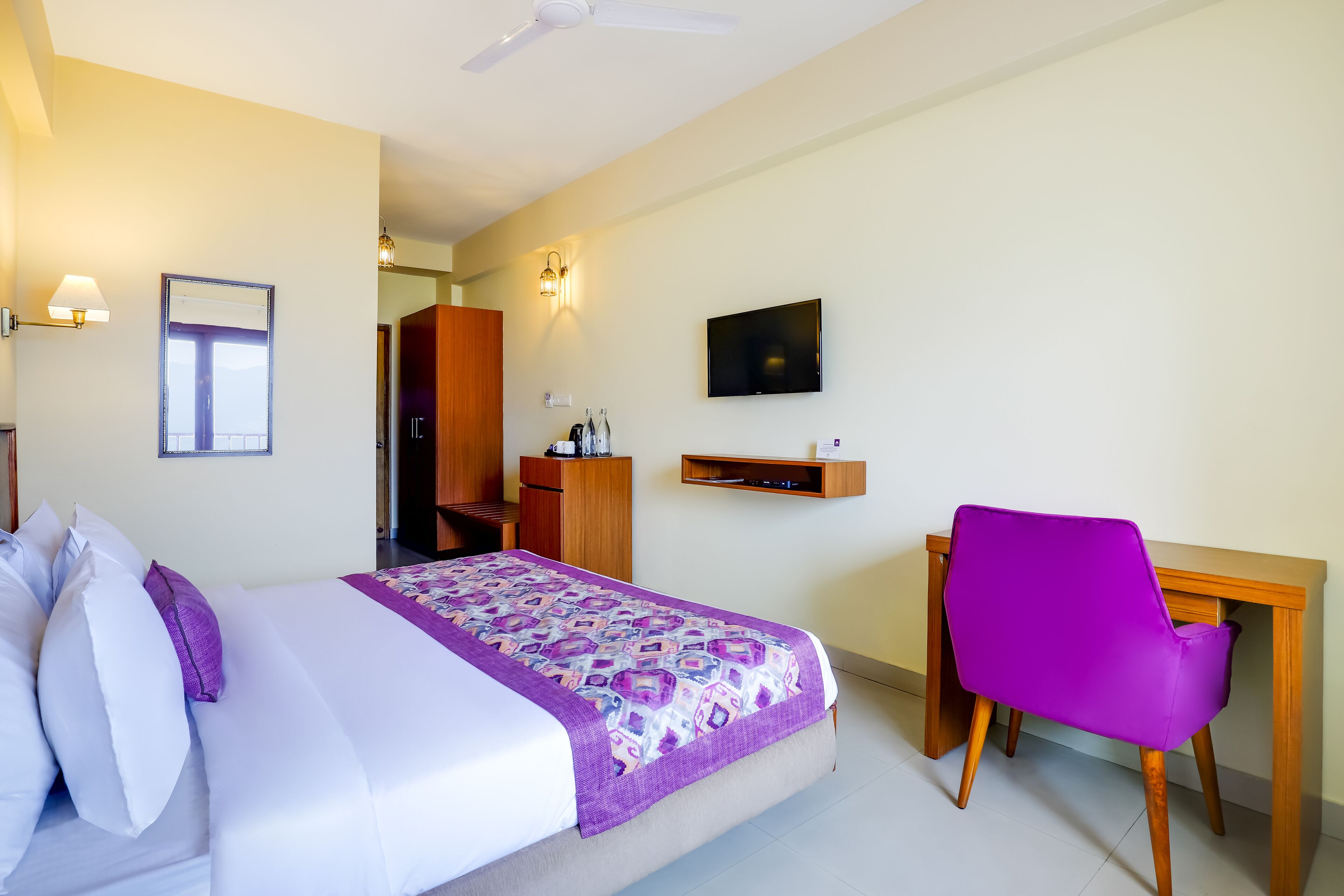 Ein Hotelzimmer mit Bett, Schreibtisch, Stuhl, Fernseher und Deckenventilator.