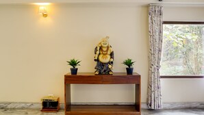 A statue on a wooden console table, two potted plants, a small heater, and a window with curtains. - Mount Himalayan Hotel (Gangtok)
