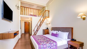 A hotel room with a bed, a nightstand, a TV, a desk, a staircase, and a wall-mounted lamp. - Mount Himalayan Hotel (Gangtok)