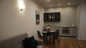 Ett kompakt bostadsutrymme med en soffa, ett matbord, stolar, ett köksområde med skåp och en liten matta.