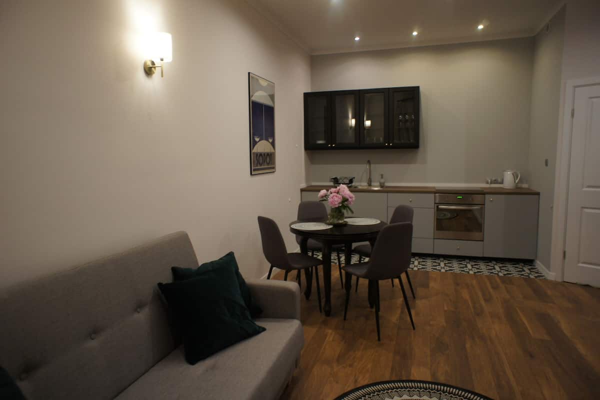 A compact living space with a sofa, dining table, chairs, a kitchen area with cabinets, and a small rug.