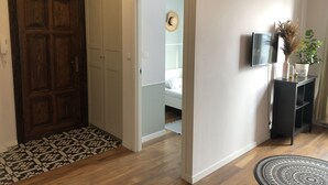 En hall med en mönstrad matta, en trädörr, en vit garderob och ett litet konsolbord med en växt och en vas.