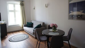 Ett modernt vardagsrum med en soffa, ett matbord med stolar, en vas med blommor och en stor, inramad tavla på väggen.
