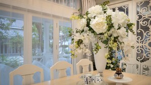A dining table with white chairs, a vase of white flowers, and a decorative teapot. - Hua Hin Beach Villa by Passionata (Hua Hin)