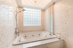 A modern bathroom with a large bathtub, a showerhead, and a window providing natural light. - Hua Hin Beach Villa by Passionata (Hua Hin)