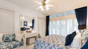A bedroom with a large bed, a smaller sofa, a vanity with a mirror, and a ceiling fan. - Hua Hin Beach Villa by Passionata (Hua Hin)
