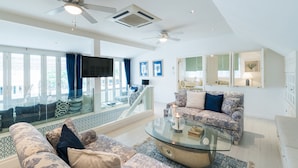 A spacious living room with a glass coffee table, patterned sofas, ceiling fans, and a view through large windows. - Hua Hin Beach Villa by Passionata (Hua Hin)