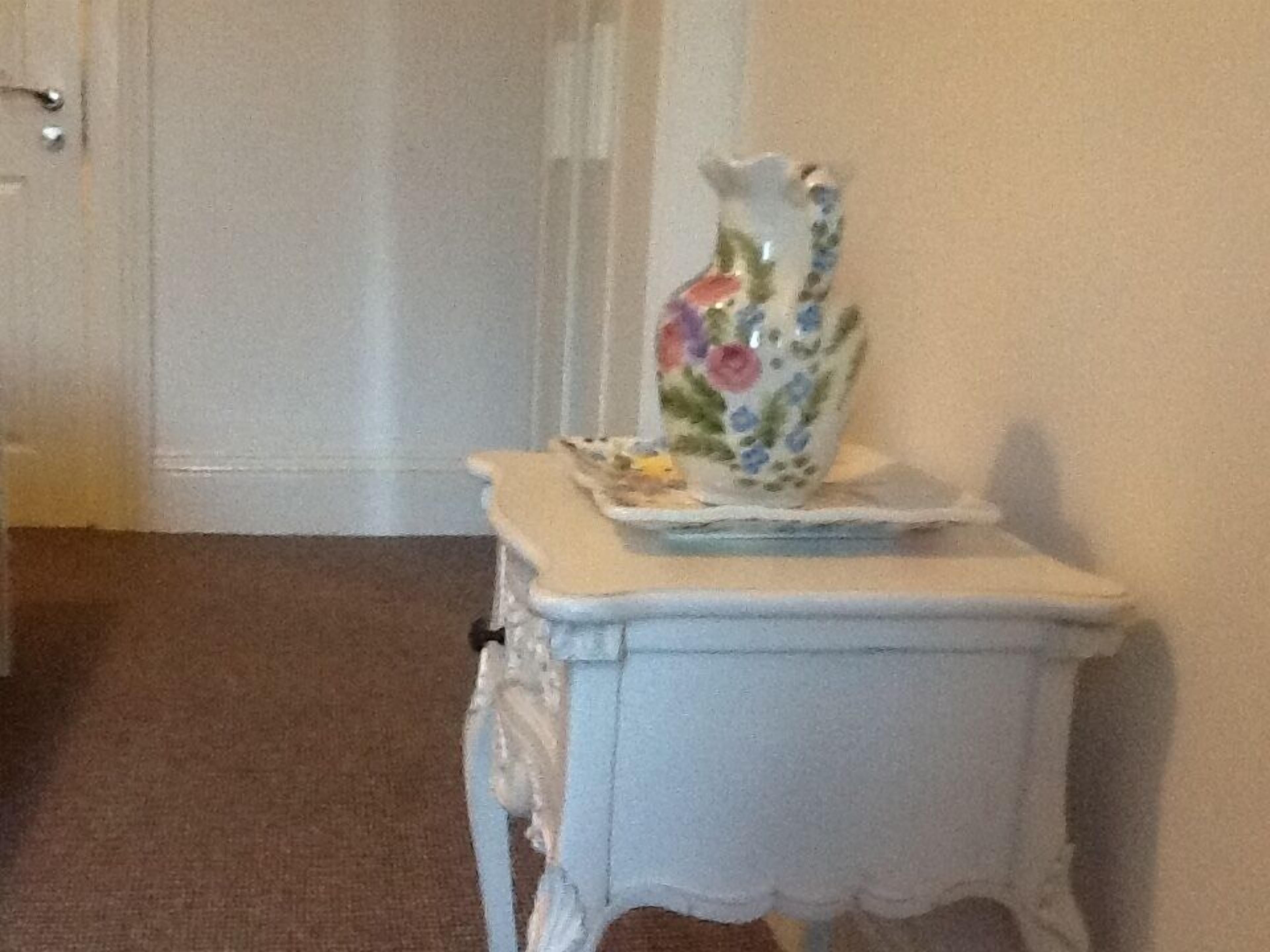 A small white table with a floral vase and a plate on top.
