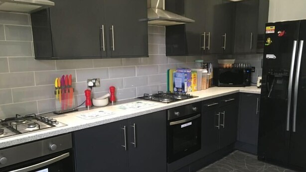 A modern kitchen with dark cabinets, a stainless steel refrigerator, a microwave, and a gas stove. - Regent Serviced Suites (Doncaster)