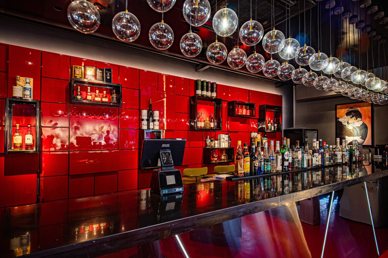 A bar with red tiled walls, a variety of liquor bottles, and a modern chandelier.