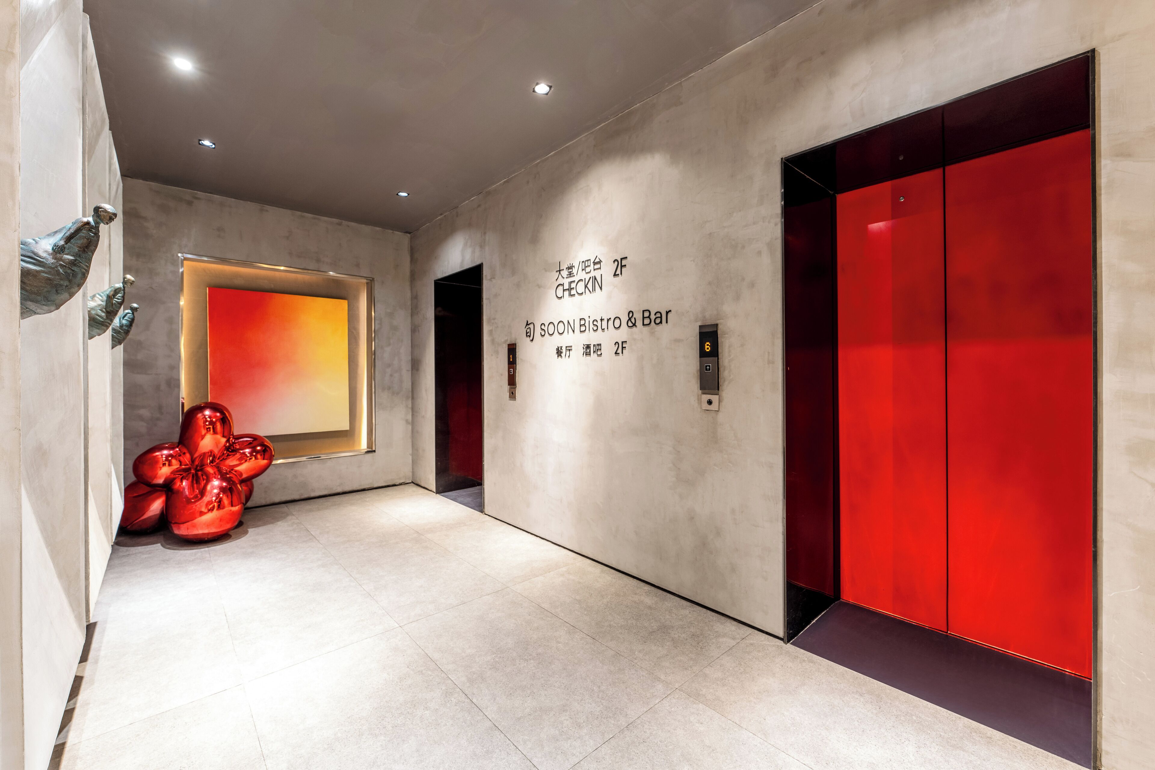 Um hall de hotel moderno com uma mesa de check-in, um bistrô e bar prestes a abrir e um elevador vermelho.