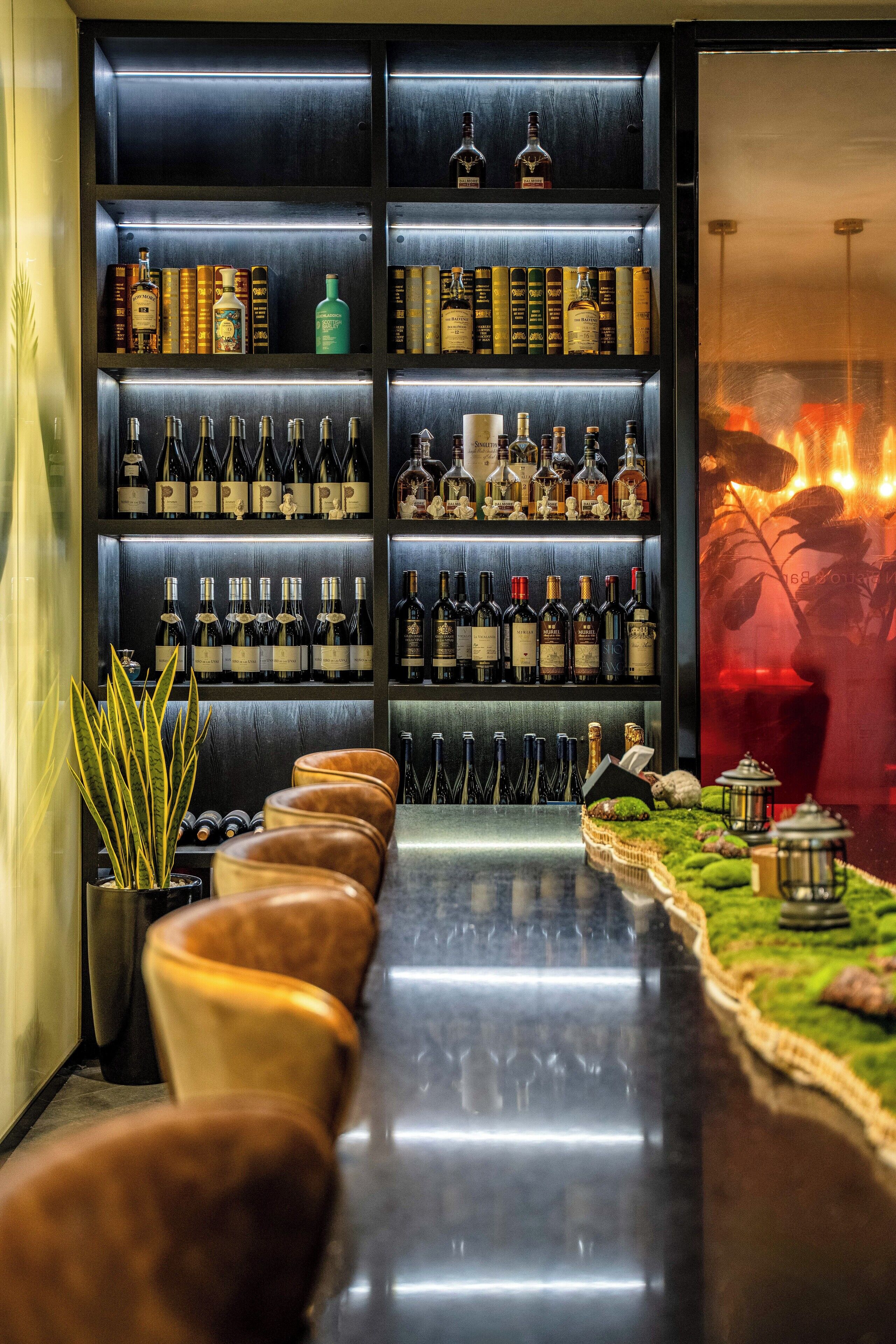 A bar area with shelves of liquor bottles, a long counter, and leather bar stools.