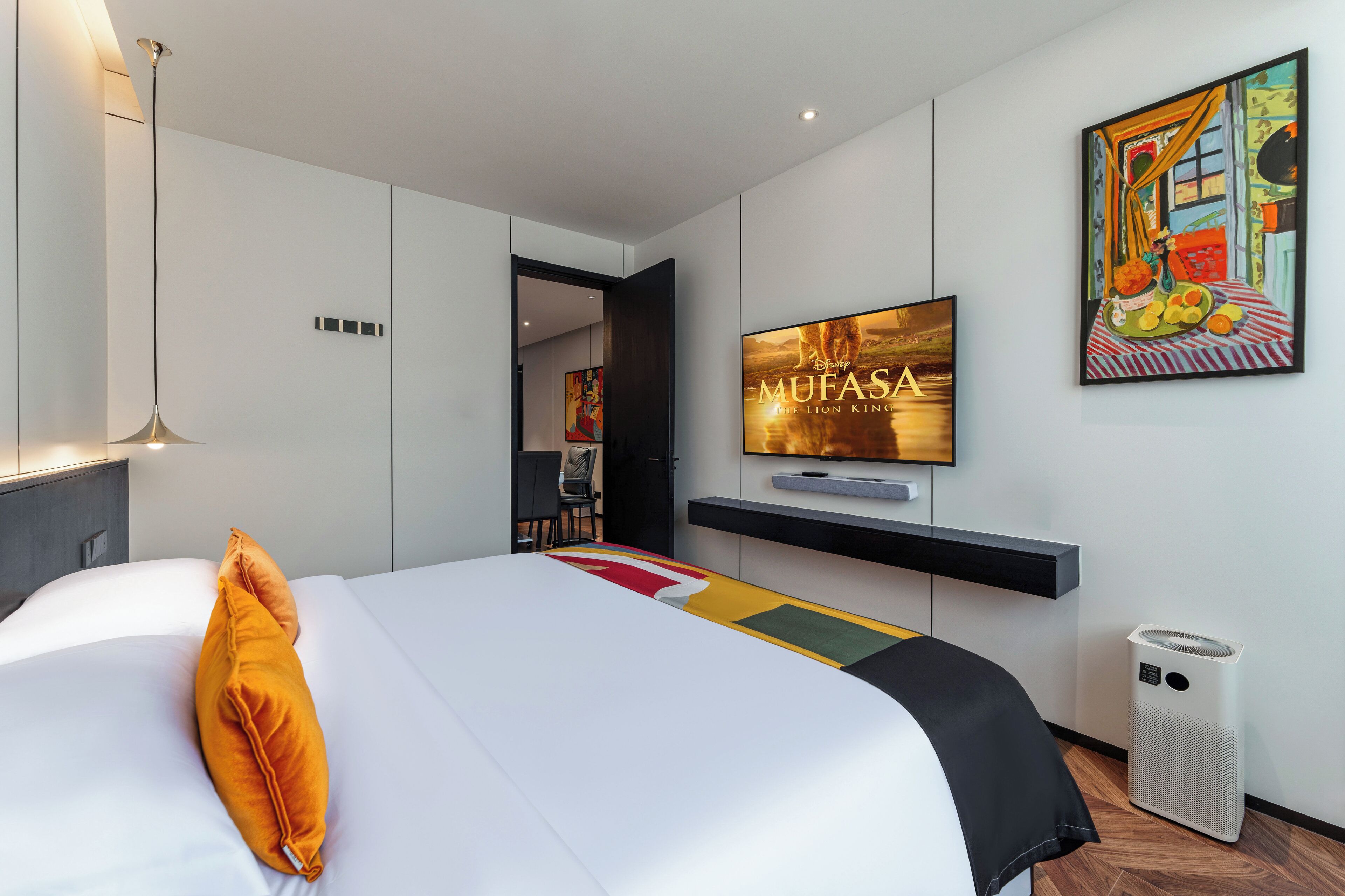 Una habitación de hotel moderna con una cama grande, un televisor montado y una obra de arte colorida en la pared.