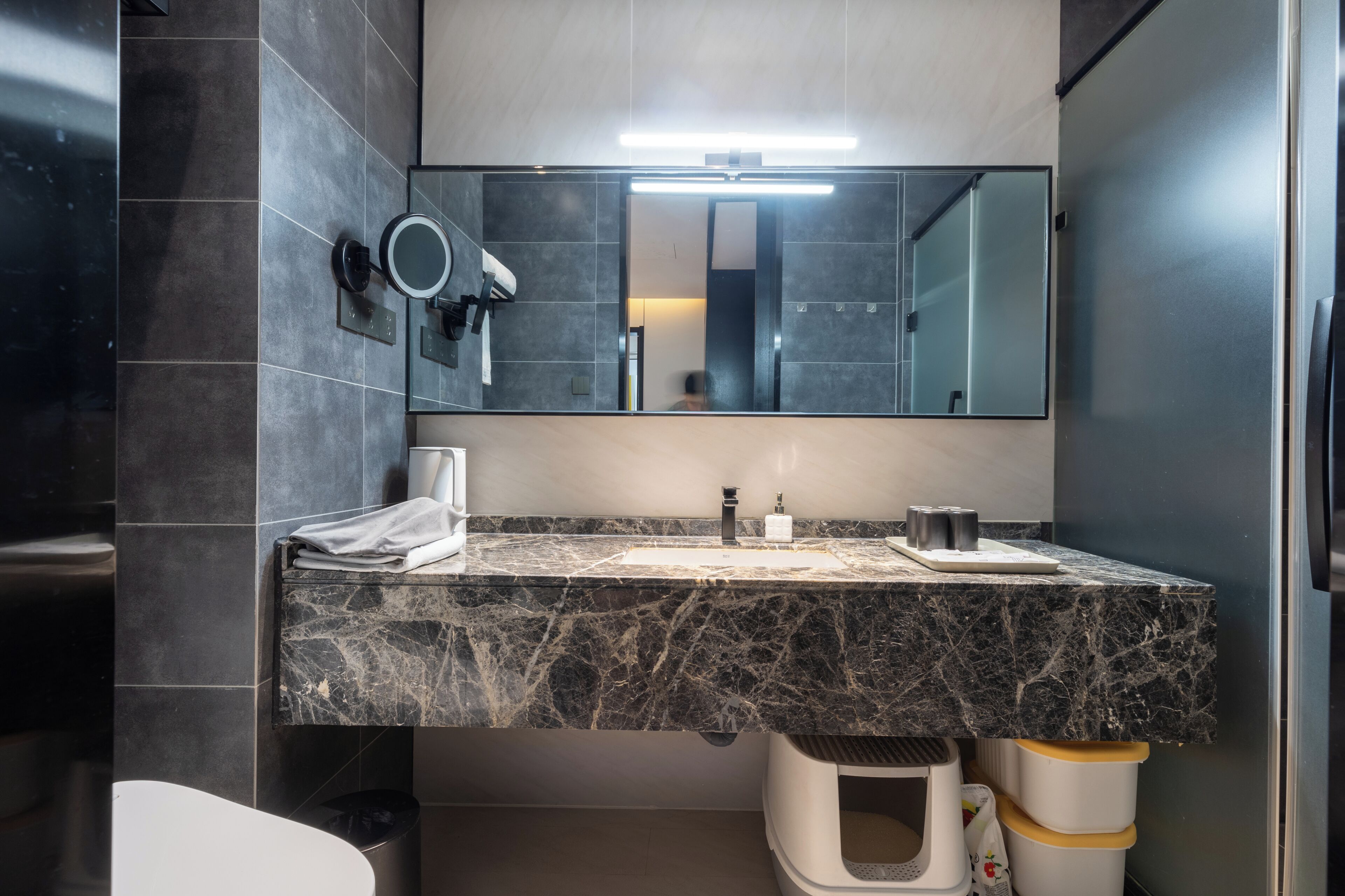 Une salle de bain moderne avec un lavabo en marbre, un grand miroir, un sèche-cheveux et une poubelle.