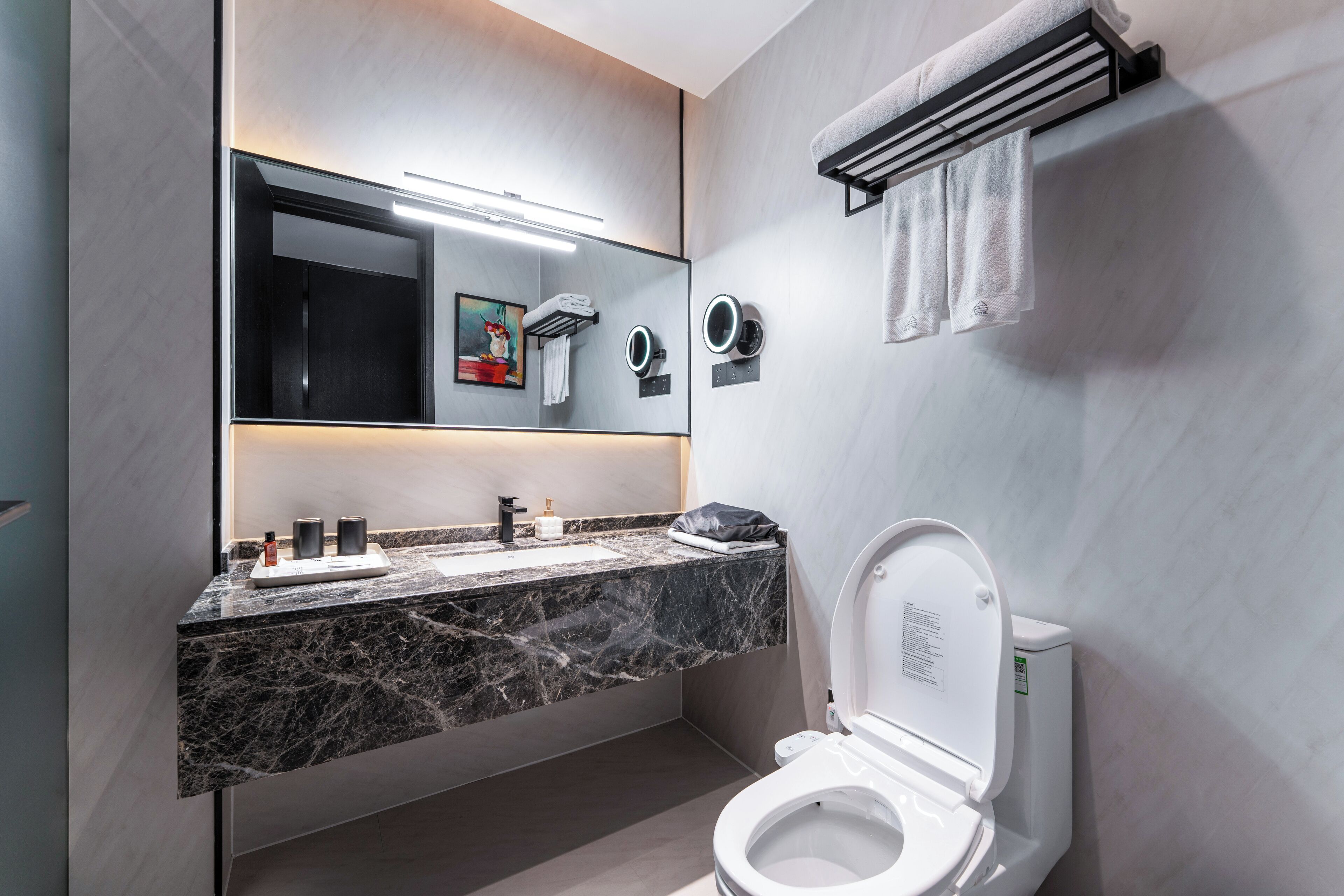 A modern bathroom with a marble countertop, a large mirror, a toilet, and a towel rack.