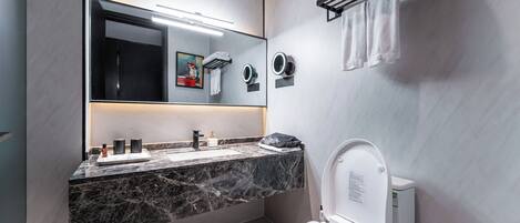 A modern bathroom with a marble countertop, a large mirror, a toilet, and a towel rack.