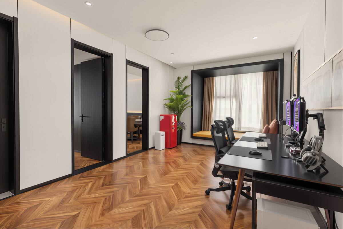 Un espace de bureau moderne avec un parquet en chevrons, une table de conférence, un bureau équipé d’un ordinateur, un meuble rouge et une plante.