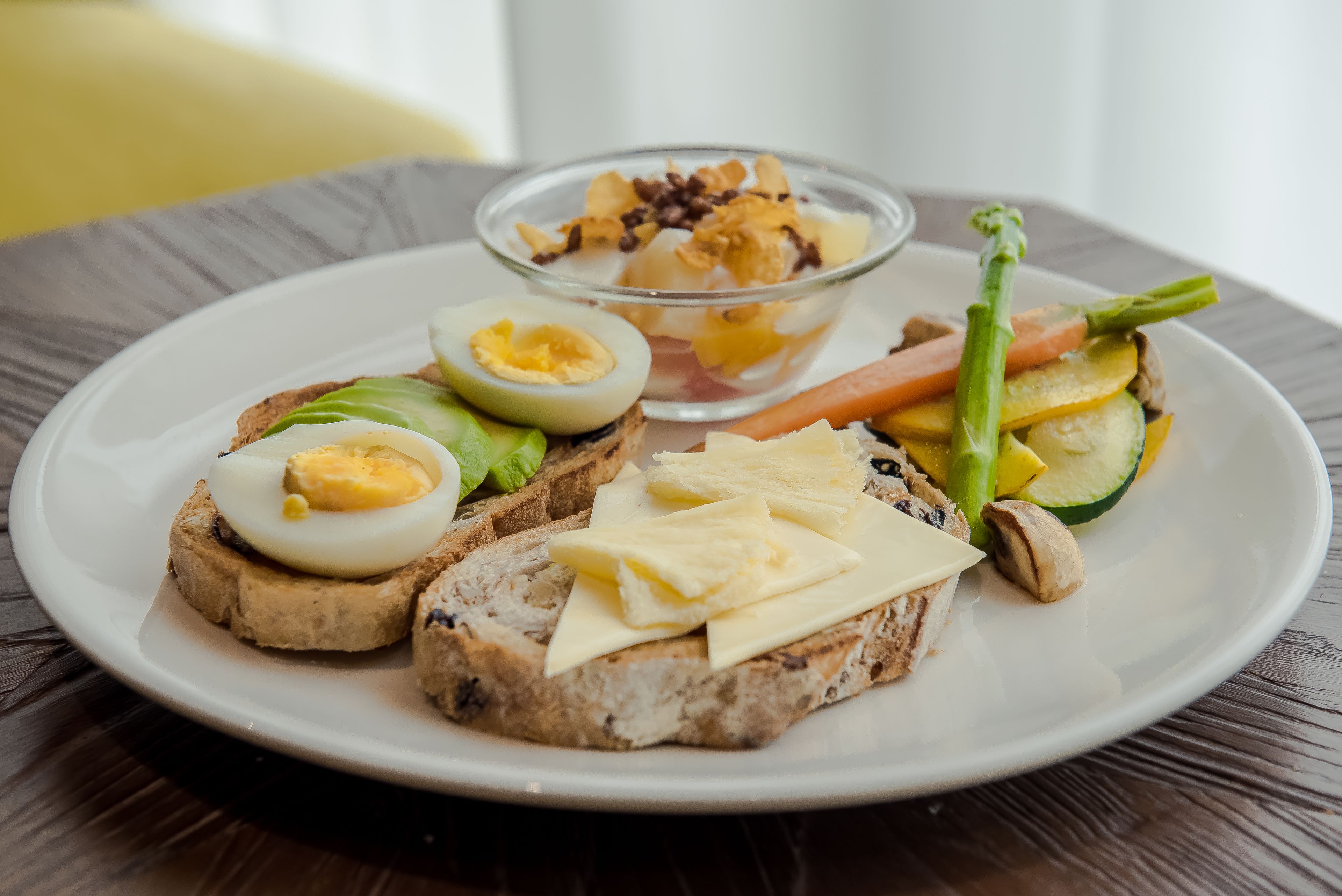 Een bord met toast, eieren, groenten en een kleine kom yoghurt met granola.