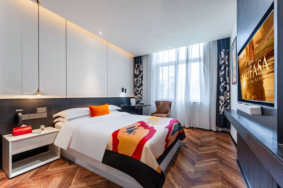 Une chambre d’hôtel moderne avec un grand lit, une table de chevet, une télévision et une vue sur le paysage urbain.