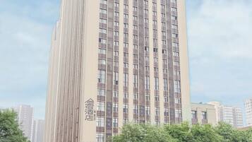 Un hotel alto y moderno con un diseño vertical llamativo, situado en una concurrida intersección urbana con movimiento en la calle y edificios circundantes.