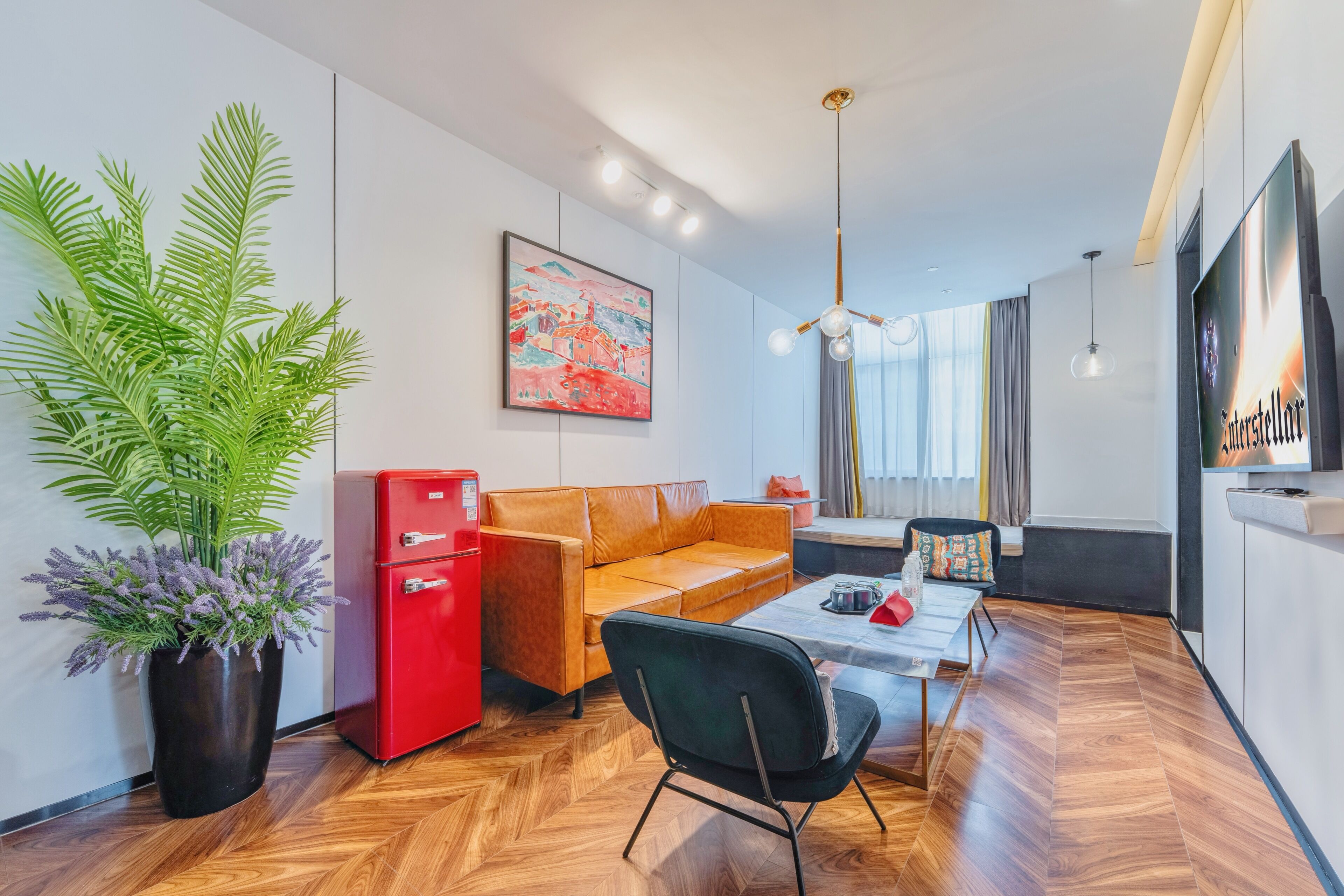 Een moderne woonkamer met een bank, een eettafel, een rode koelkast, een potplant en een schilderij aan de muur.