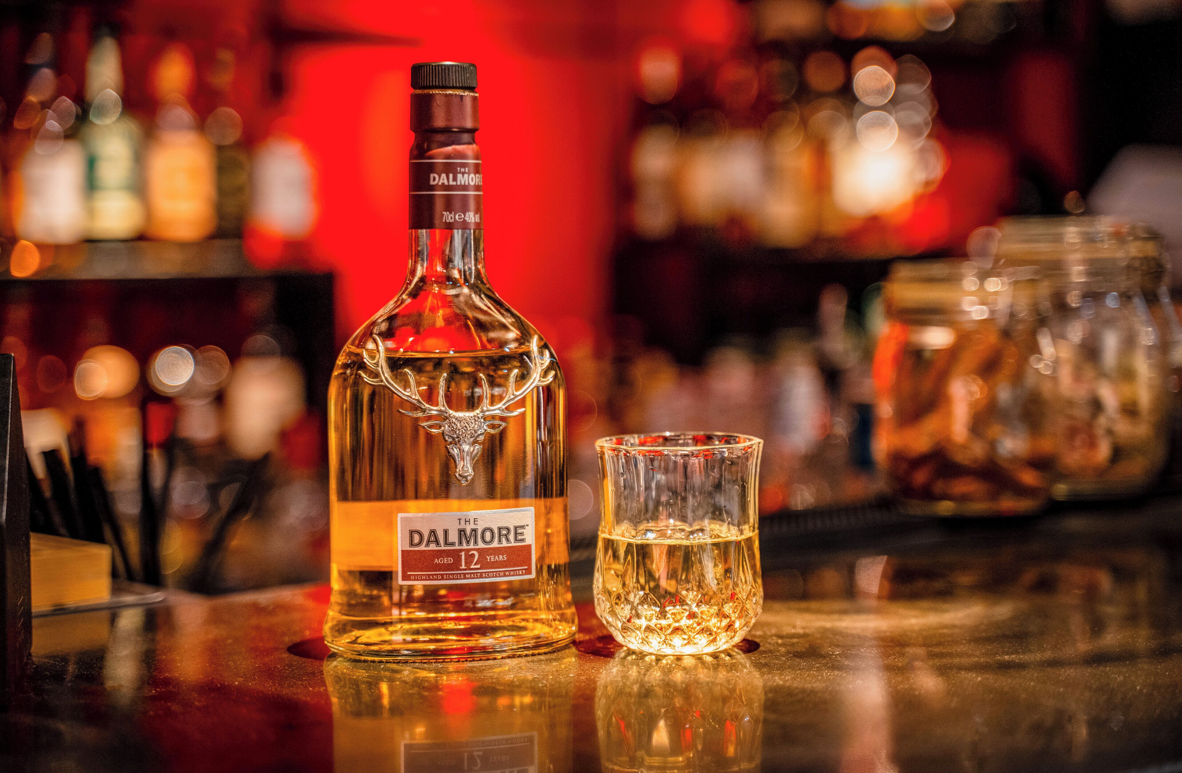 A bottle of Dalmore whisky and a glass on a bar counter.