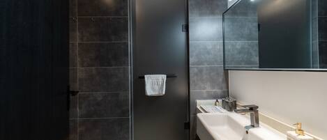 A modern bathroom with dark tiles, a white sink, and a towel hanging on a door.