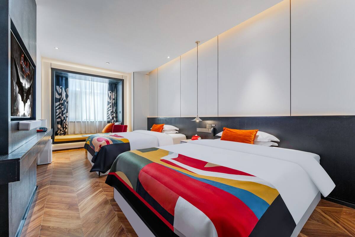 Une chambre d’hôtel moderne avec deux lits, une grande fenêtre avec des rideaux légers, un plancher en bois et un téléviseur fixé au mur.