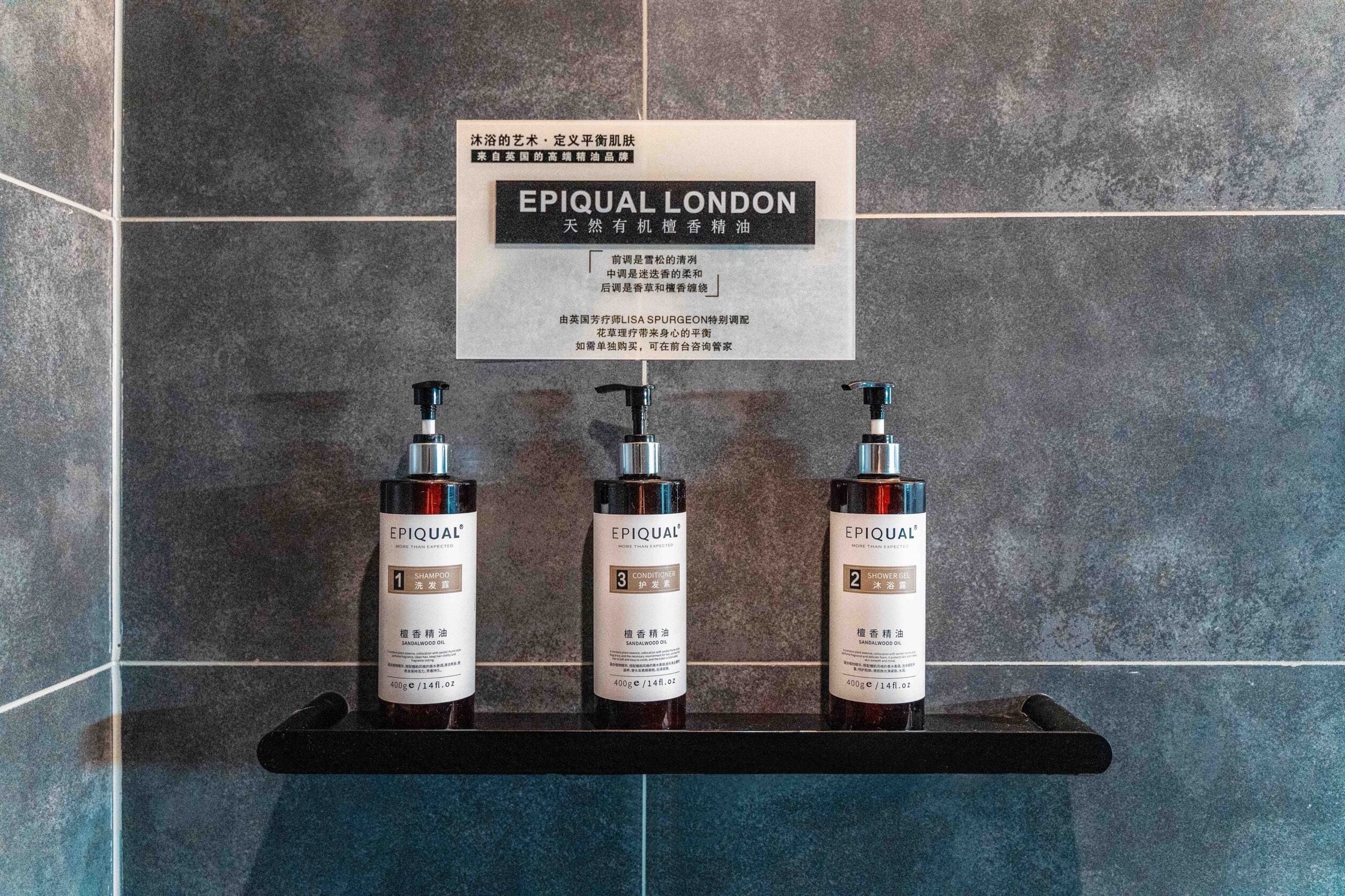 A bathroom with a sign above a shelf displaying three bottles of EPIQUAL London products.