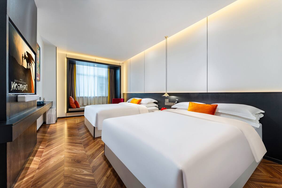 Une chambre d’hôtel avec deux lits, une télévision, un bureau et une fenêtre avec des rideaux.