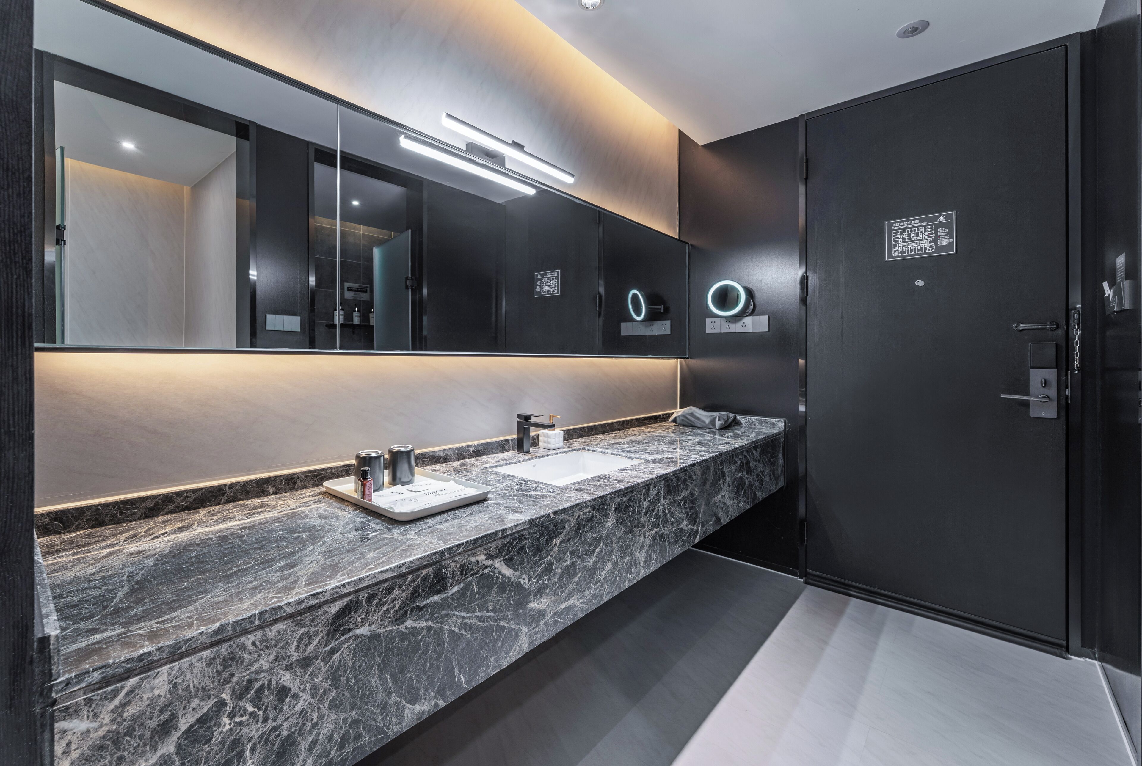 Un baño moderno con encimera de mármol, dos lavamanos, un espejo grande y una puerta oscura.