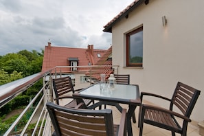 A balcony with a table and chairs, overlooking a red-roofed building and greenery. - Imperial Apartments - Martini (Sopot)