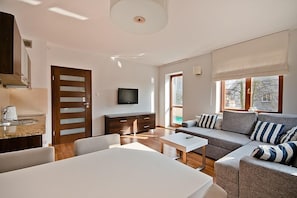 A modern living room with a sofa, a dining table, and a kitchen area with a stove and cabinets. - Imperial Apartments - Martini (Sopot)
