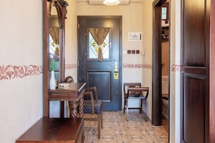 Un vestíbulo de hotel con un mostrador de recepción de madera, sillas, una puerta de madera oscura con ventanal y un piso de baldosas.