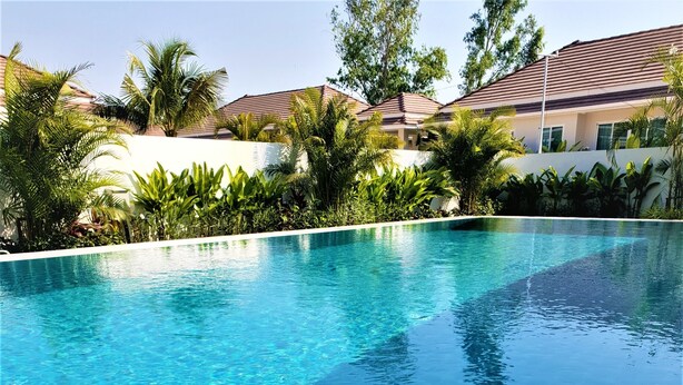 A swimming pool with clear blue water, surrounded by a pebble border and lush greenery. - Villa de Veluwe at Hua Hin (Hua Hin)