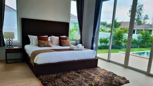 A bedroom with a large bed, a nightstand, a rug, and a view of a swimming pool and greenery. - Villa de Veluwe at Hua Hin (Hua Hin)