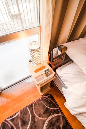 Et hotelværelse med en seng, et sengebord med lampe, et spejl og et vindue med gardiner.