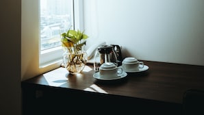 Une table avec une plante, une machine à café et des tasses près d’une fenêtre.