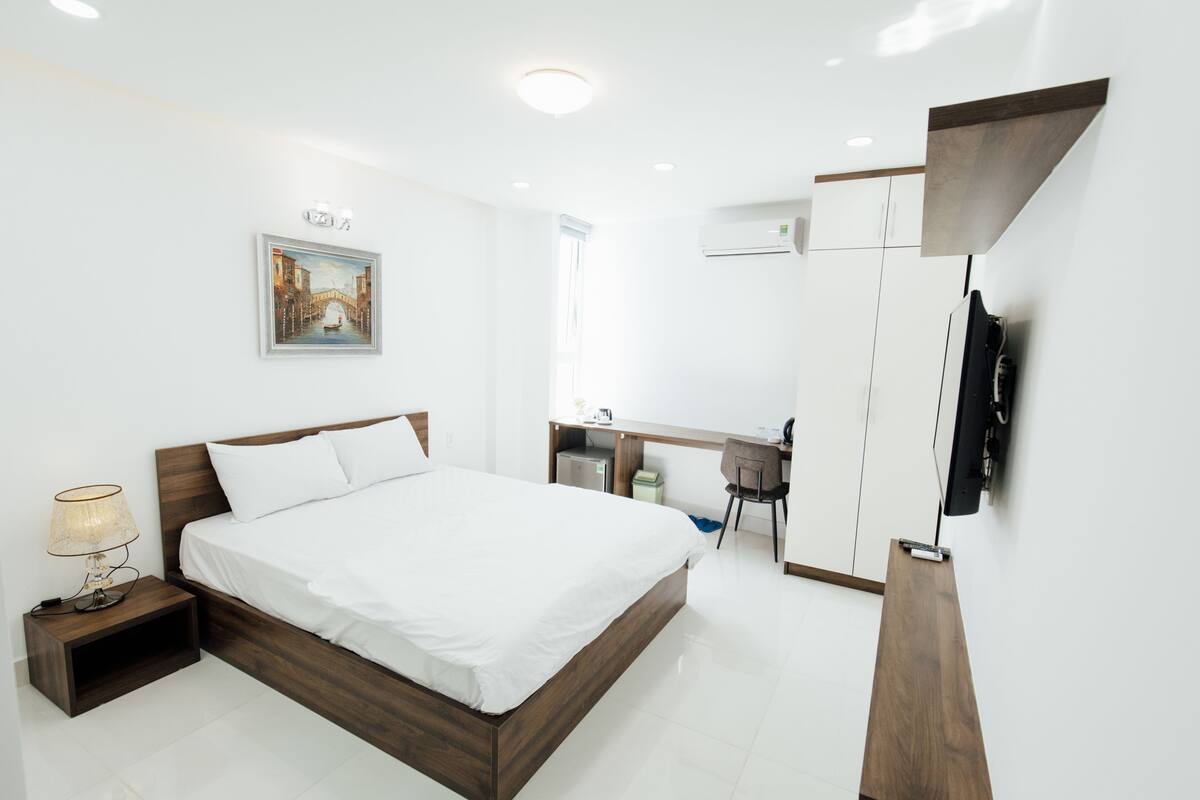 Ein modernes Hotelzimmer mit einem hölzernen Bett, einem Schreibtisch mit Stuhl, einem Flachbildfernseher und einem Bild an der Wand.