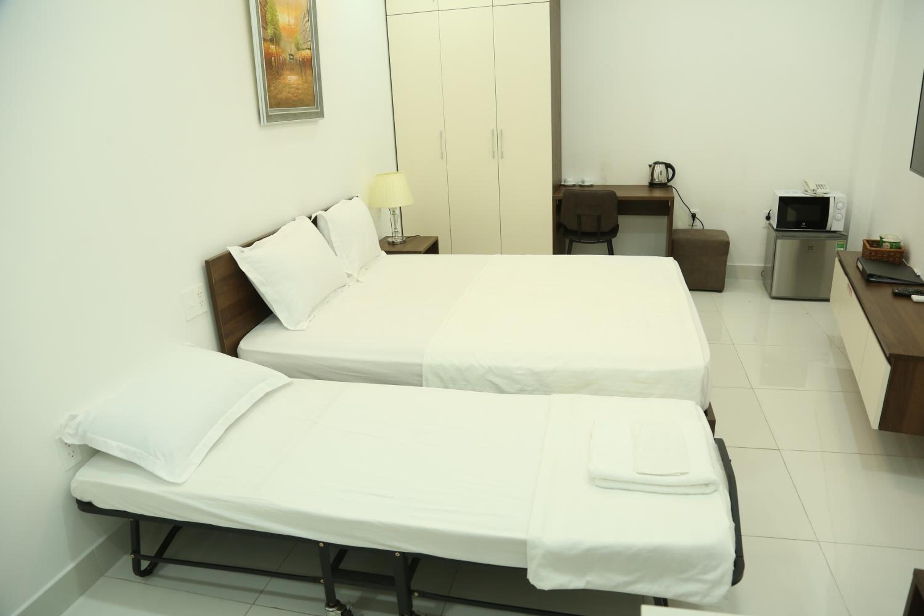 Ein Hotelzimmer mit zwei Einzelbetten, einem Schreibtisch mit Stuhl, einer Mikrowelle und einem kleinen Kühlschrank.