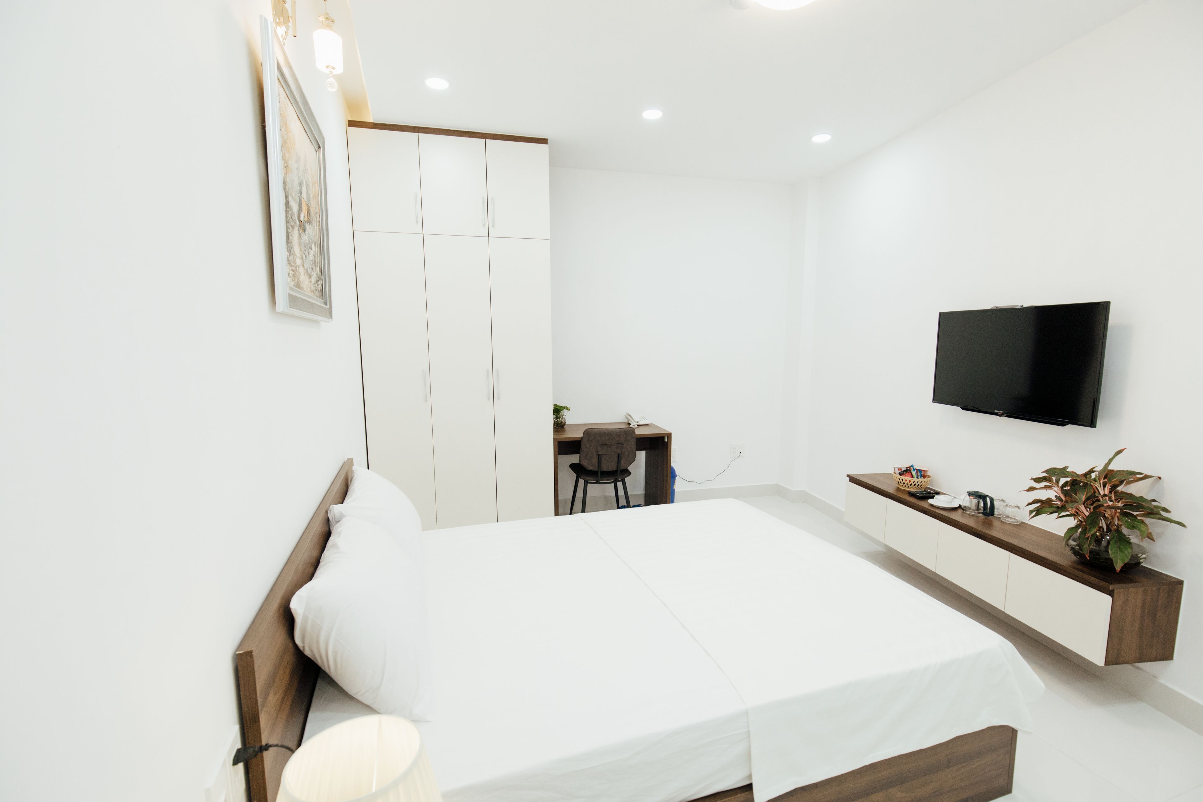 A modern bedroom with a bed, bedside table, TV, and a desk with a chair.