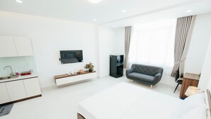 Une chambre d’hôtel moderne dotée d’un grand lit, d’un canapé, d’un téléviseur fixé au mur et d’un petit coin cuisine.