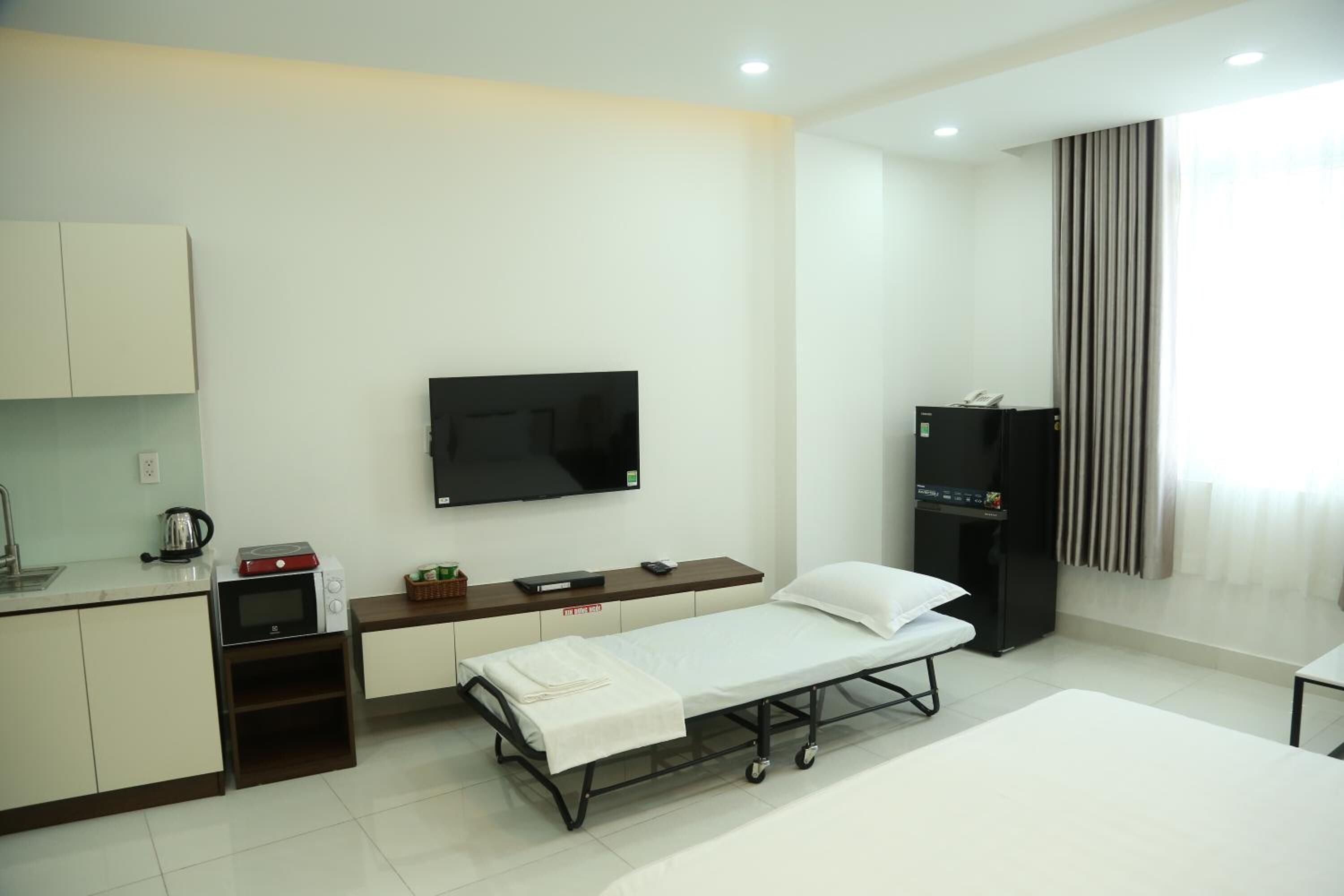 Ein sauberes, modernes Hotelzimmer mit Bett, kleinem Schreibtisch, Flachbildfernseher, Küchenzeile und Kleiderschrank.