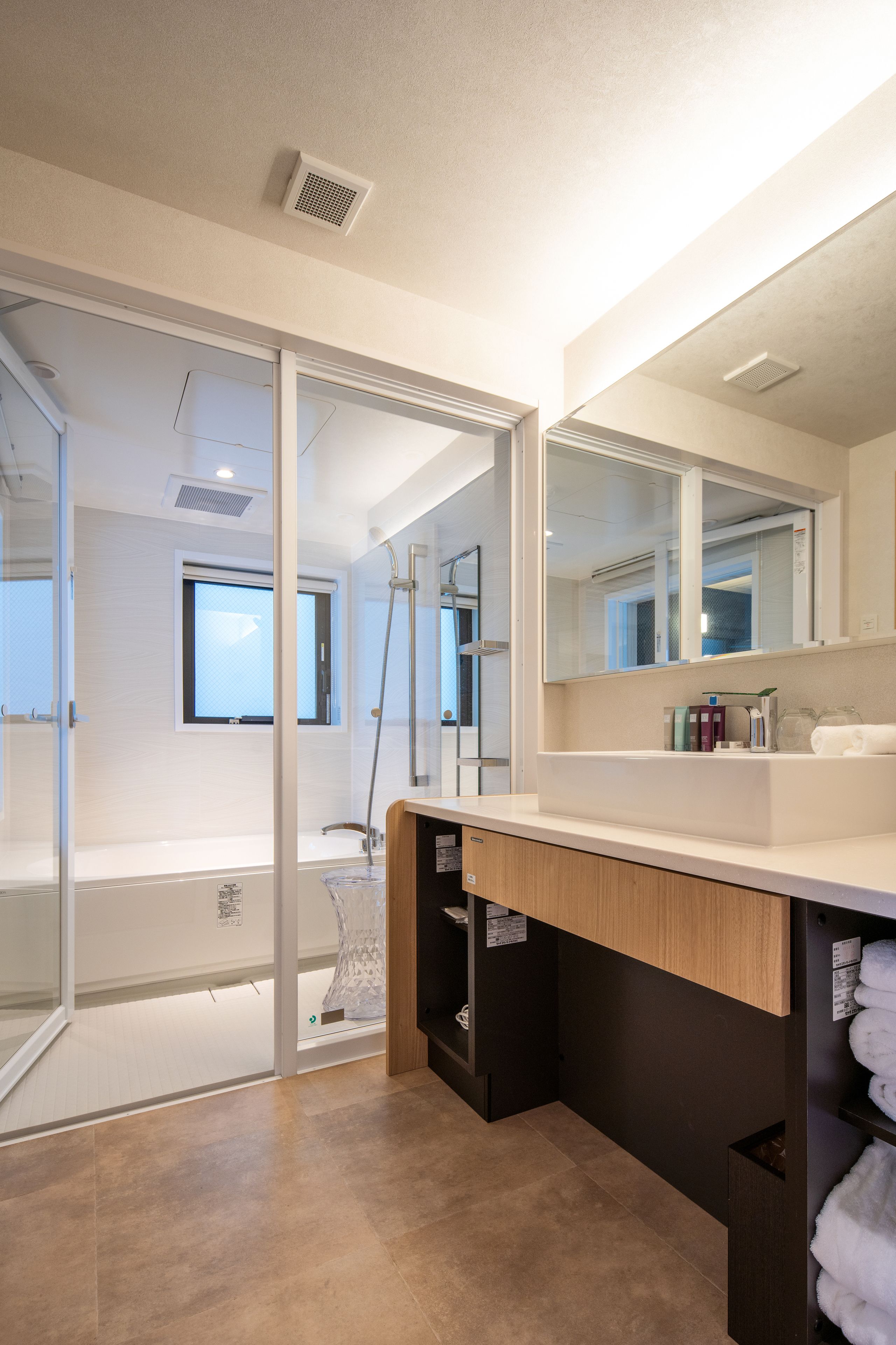 A modern bathroom with a glass shower enclosure, a large mirror, and a wooden vanity.