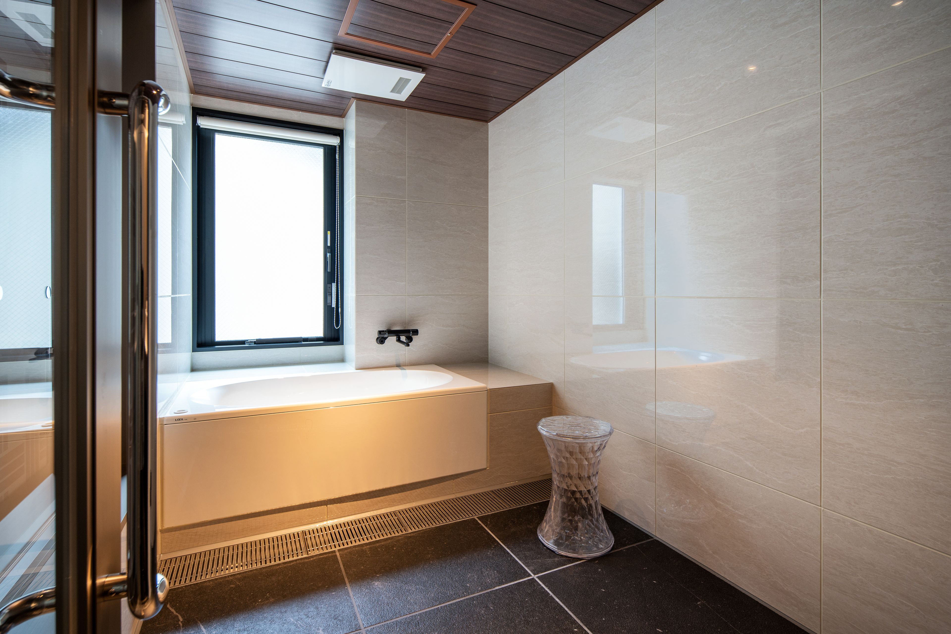 Un baño moderno con bañera, una ventana y un taburete de vidrio.