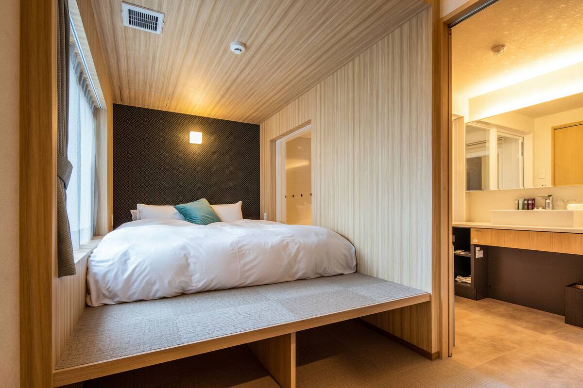 A bedroom with a bed, a bench, a window, and a bathroom with a mirror.