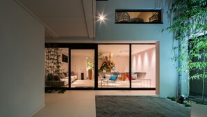 Un espacio interior con diseño moderno, que cuenta con un gran ventanal corredero que da a una sala de estar con sofá, mesa de centro y una planta decorativa.