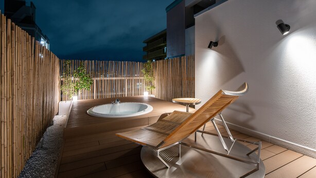 Una terraza de madera con un jacuzzi, una silla de descanso y una mesita.