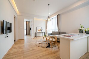 A modern living room with a wooden floor, a sofa, a dining table with chairs, a TV mounted on the wall, and a pendant light. - Suisse Place Shanghai (Shanghai)